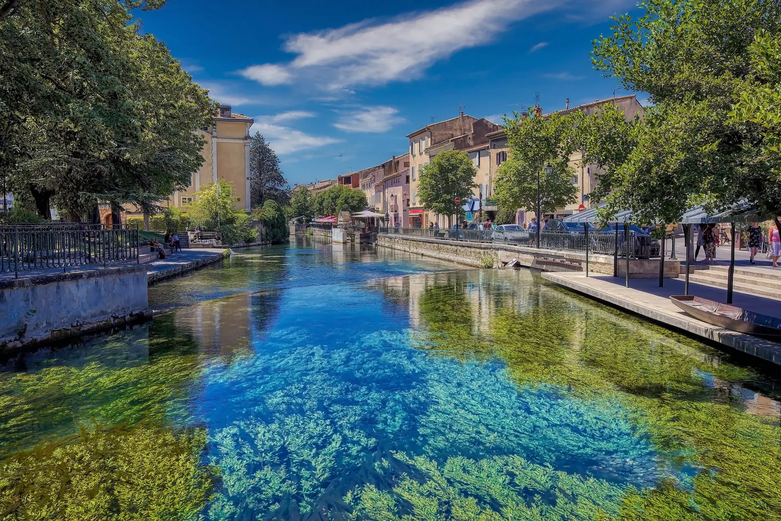 O rio Sorgue, límpido e turquesa, que atravessa L’Isle-sur-la-Sorgue, com as suas algas a ondular sob a água, cais arborizados e fachadas em tons pastel