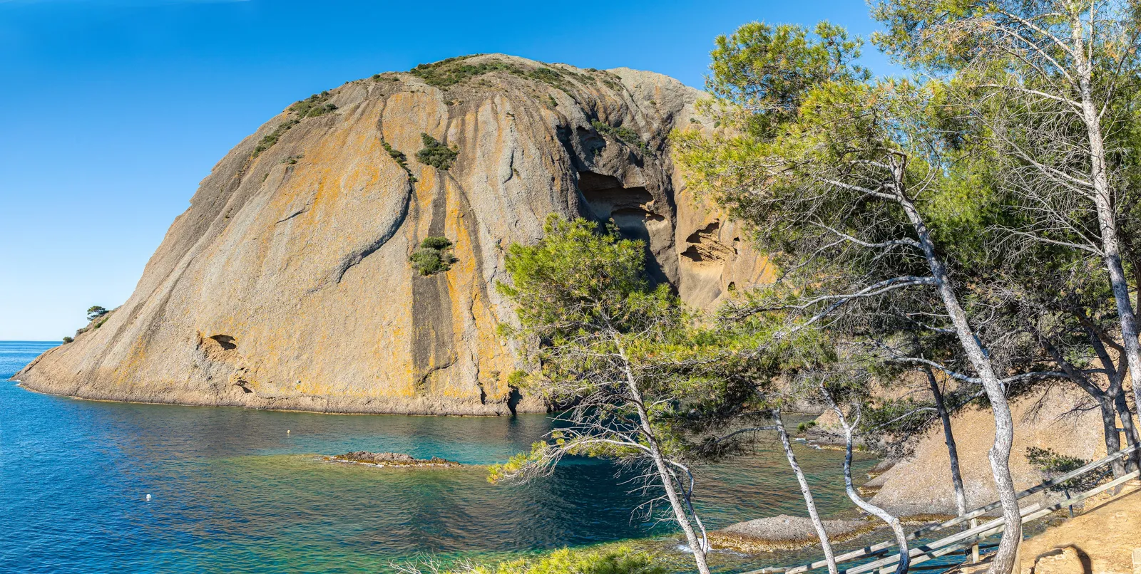 La calanque du Grand Mugel à La Ciotat au lever du soleil, son grand rocher et les pins penchés au-dessus de l’eau claire