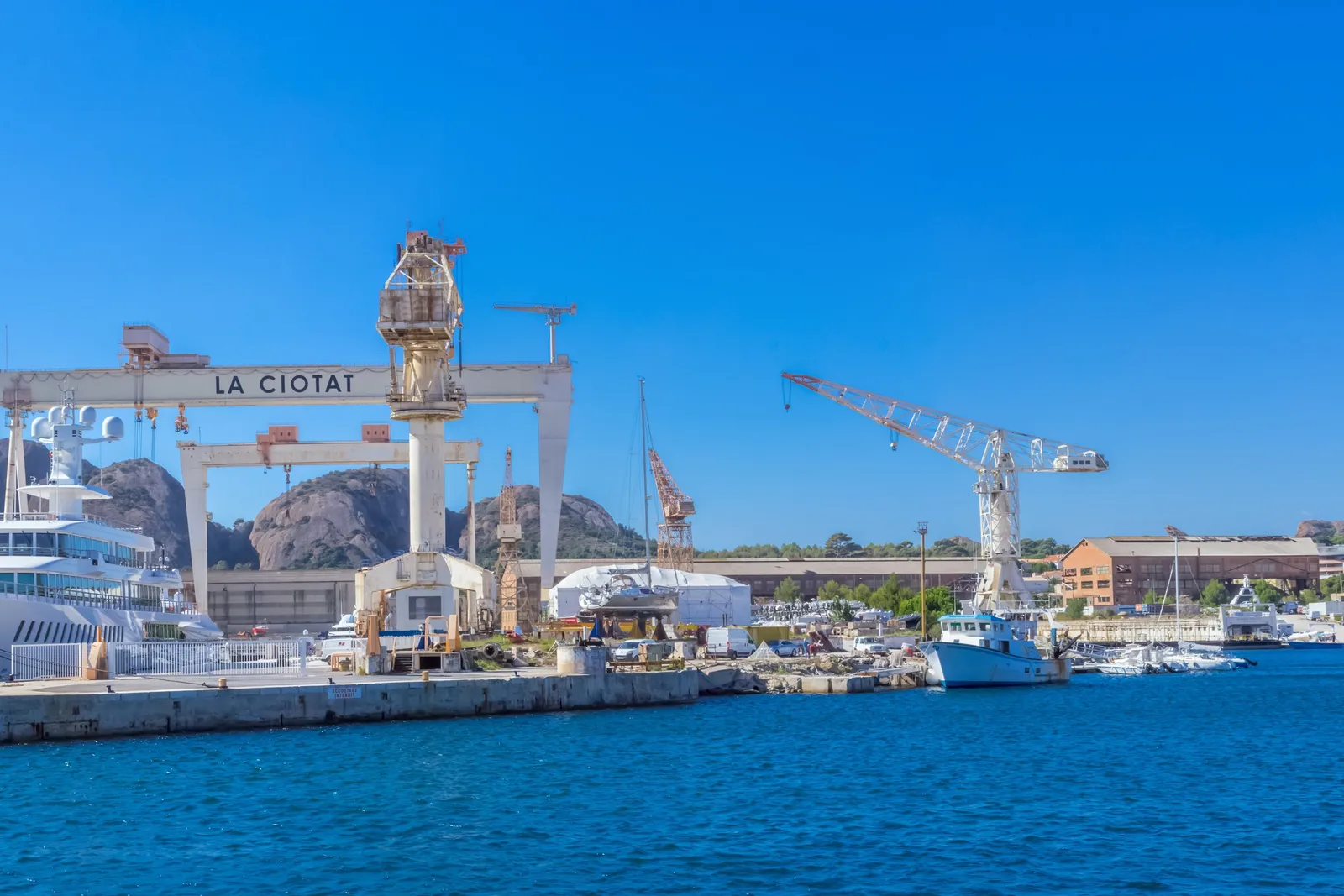 Os estaleiros de La Ciotat e o seu grande pórtico, um iate atracado diante dos rochedos do Bec de l’Aigle