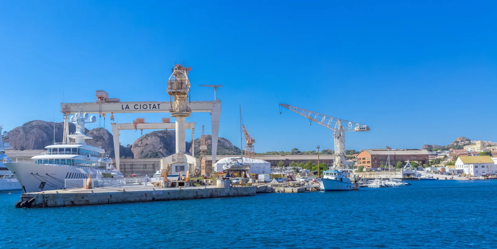 Os estaleiros de La Ciotat e o seu grande pórtico, um iate atracado diante dos rochedos do Bec de l’Aigle