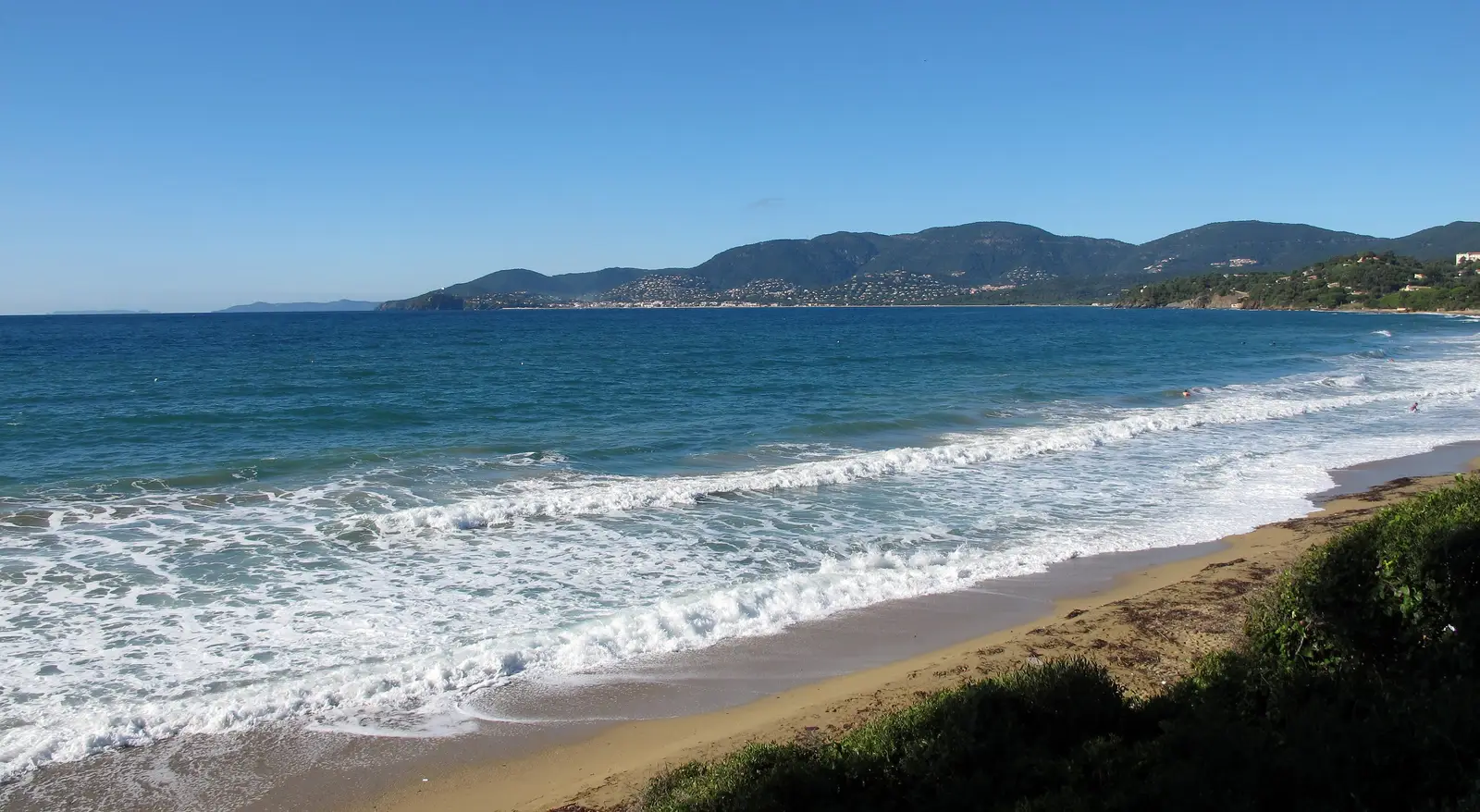 A praia de Gigaro em La Croix-Valmer, as suas ondas na areia e as colinas arborizadas até ao fundo da baía