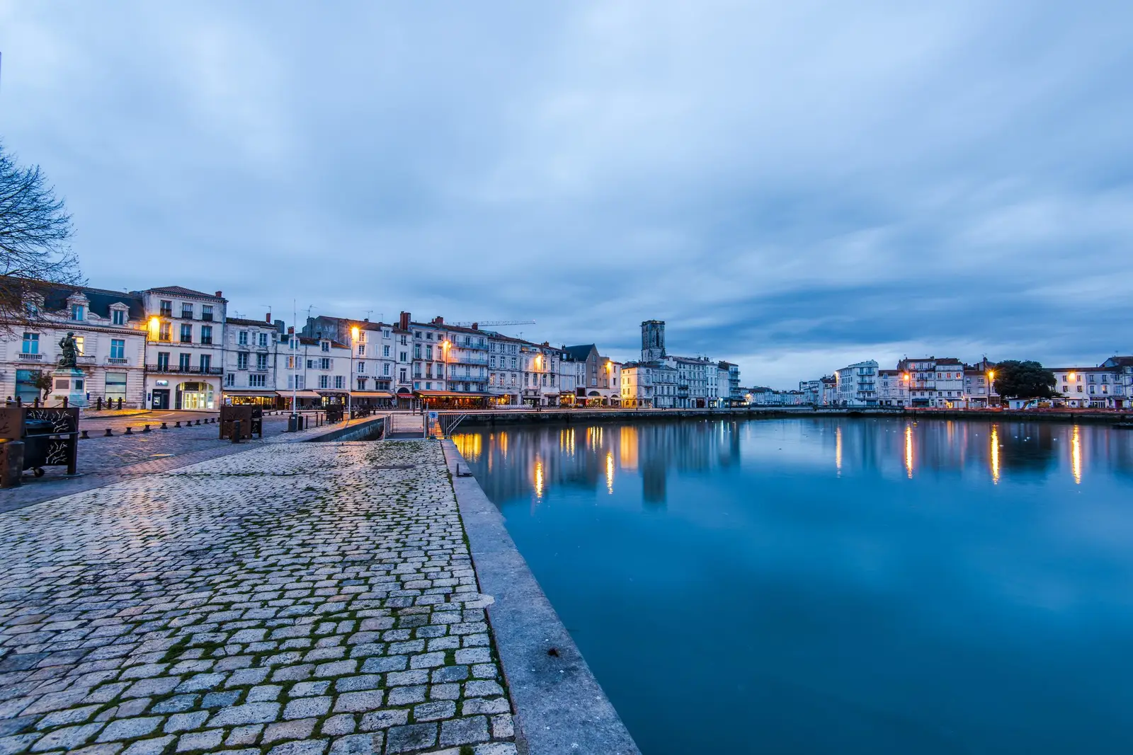 As fachadas dos cais do Vieux-Port de La Rochelle ao crepúsculo, refletidas na bacia, calçada em primeiro plano