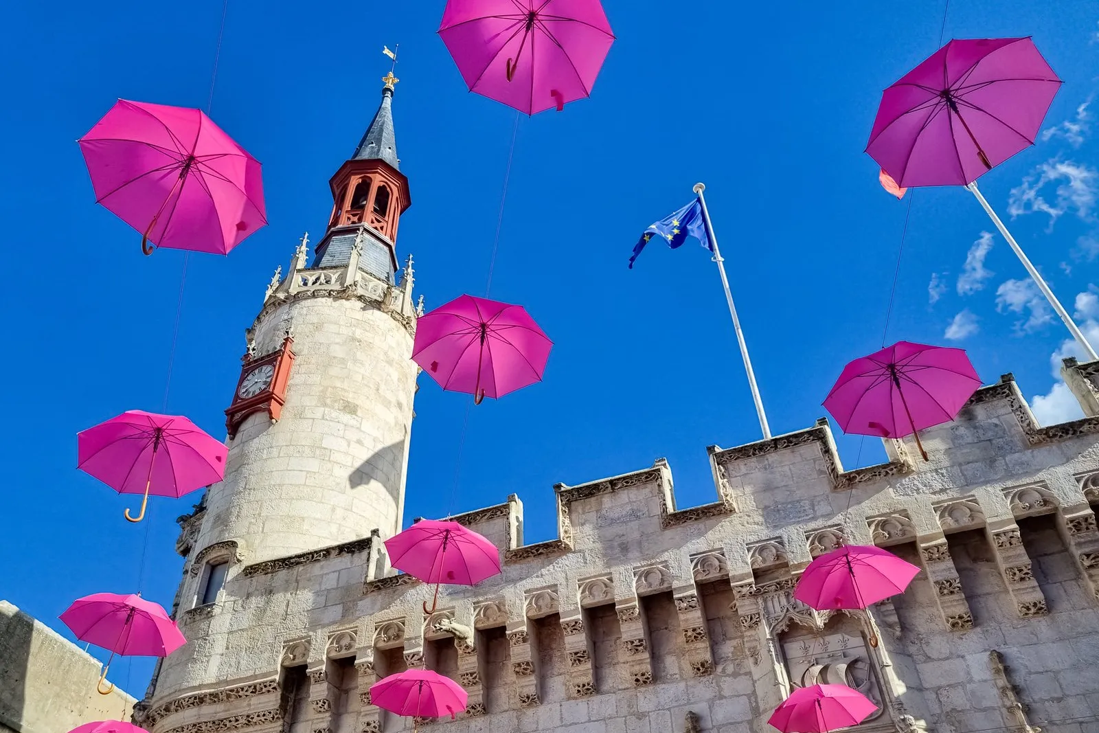 A porta da Grosse Horloge de La Rochelle sob uma revoada de guarda-chuvas cor-de-rosa