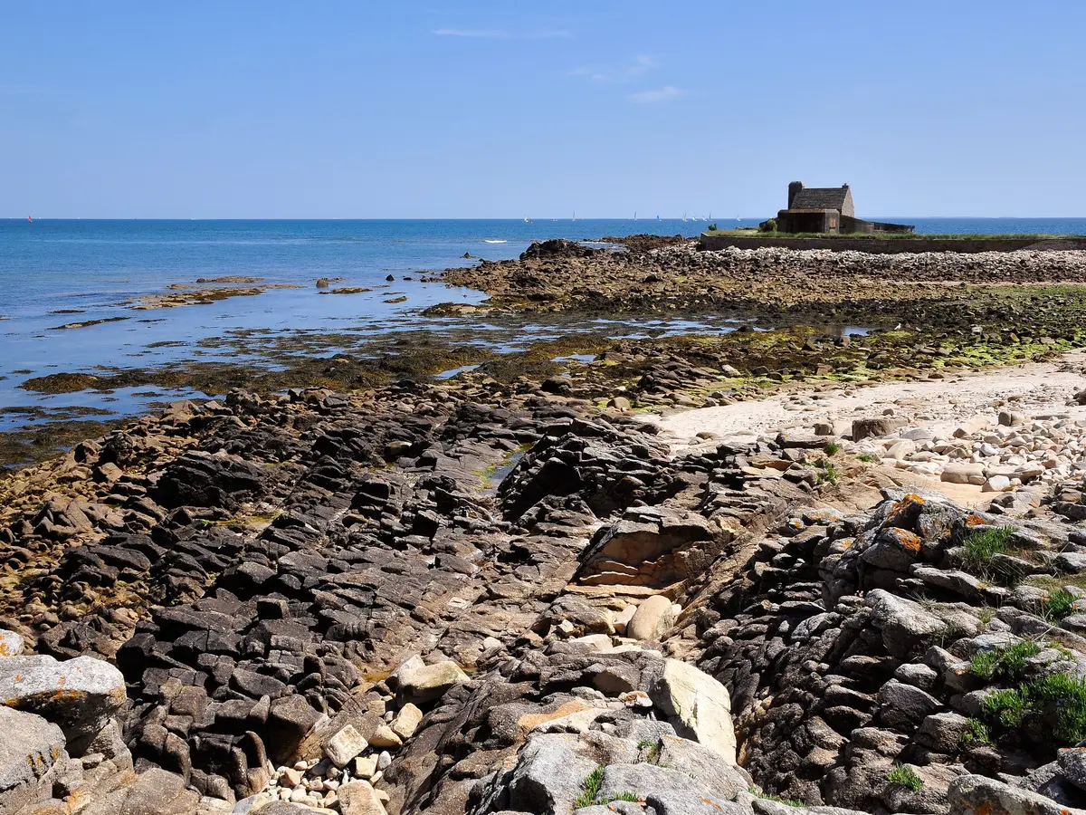 La côte rocheuse de La Trinité-sur-Mer à marée basse, ses roches plates et un petit abri de pierre au bout de la pointe, face à la baie