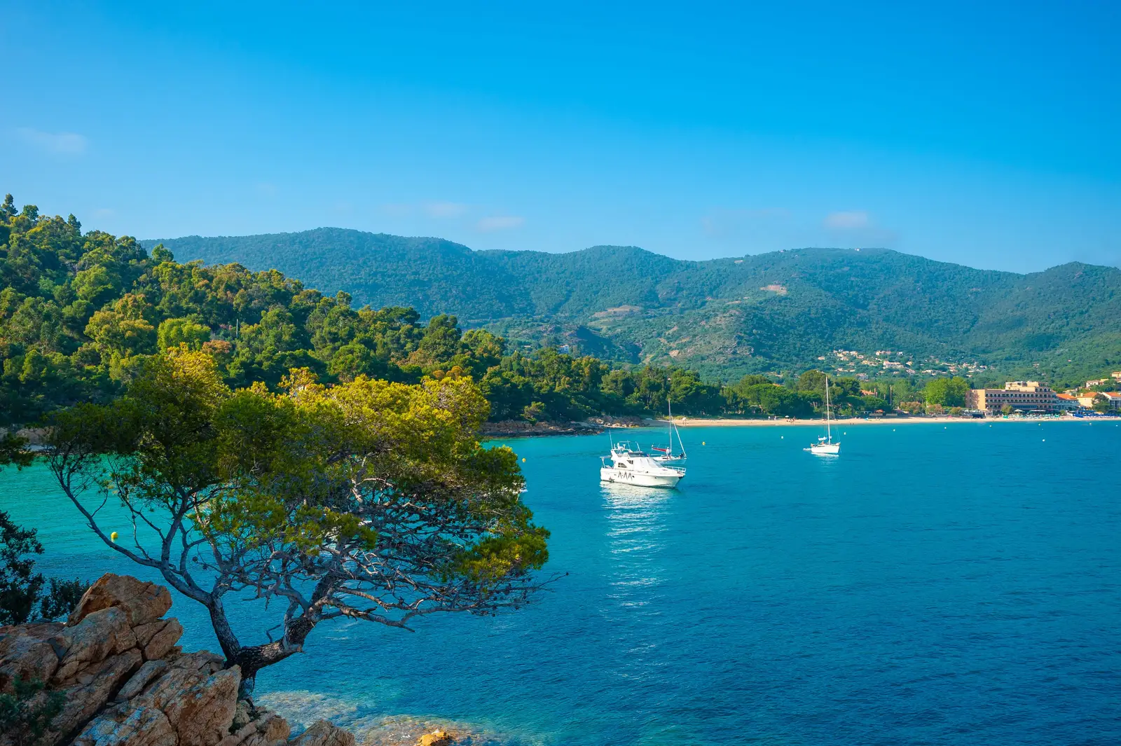 Le littoral du Layet, au Lavandou : la mer turquoise, des bateaux au mouillage et les collines des Maures