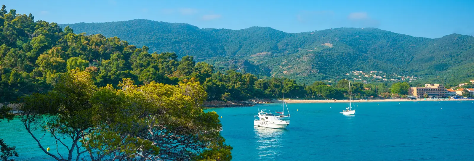 Le littoral du Layet, au Lavandou : la mer turquoise, des bateaux au mouillage et les collines des Maures