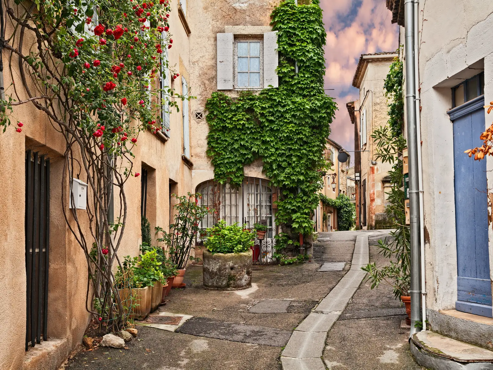 Uma ruela florida na aldeia de Lourmarin, as suas fachadas ocre, as suas roseiras e a sua trepadeira à volta de uma bacia de pedra