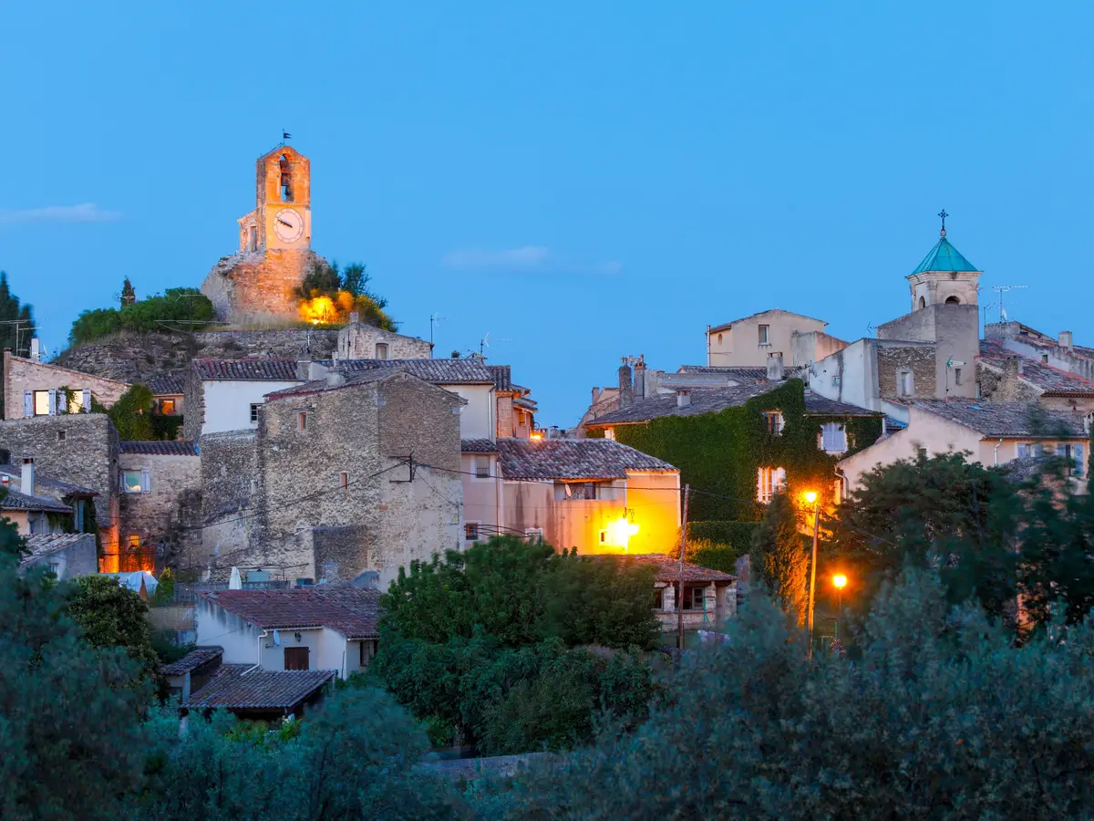 Lourmarin ao cair da noite, a aldeia iluminada, o seu campanário e a torre do relógio acima das oliveiras