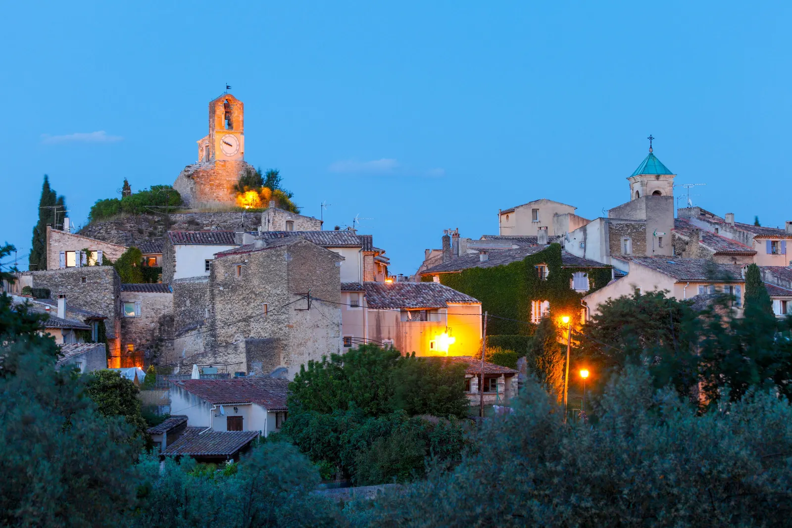 Lourmarin at dusk, the village lit up, its belfry and bell tower above the olive trees