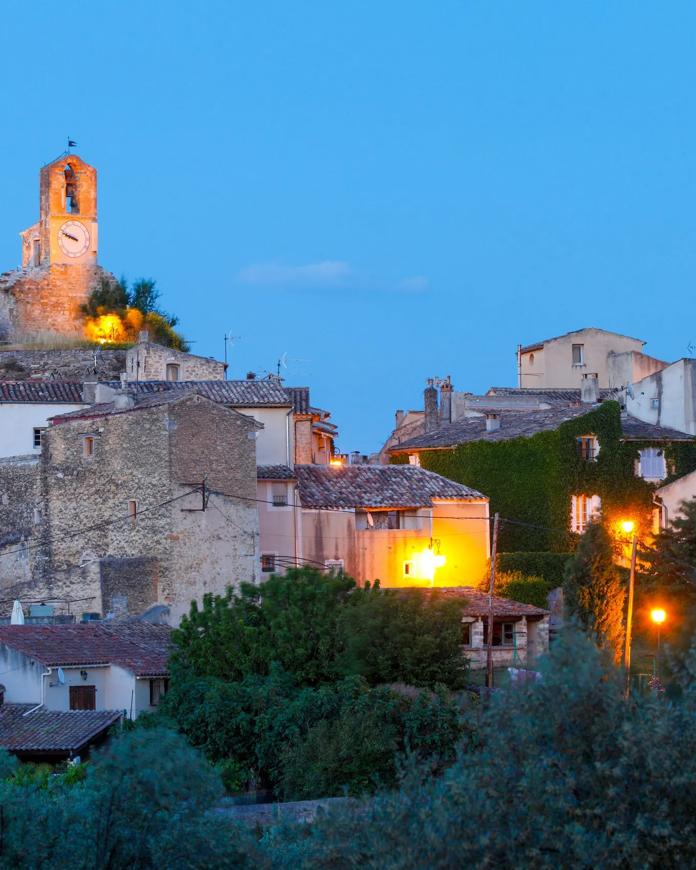 Lourmarin at dusk, the village lit up, its belfry and bell tower above the olive trees