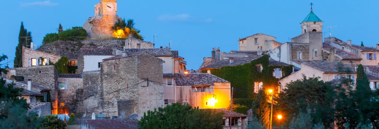 Lourmarin at dusk, the village lit up, its belfry and bell tower above the olive trees