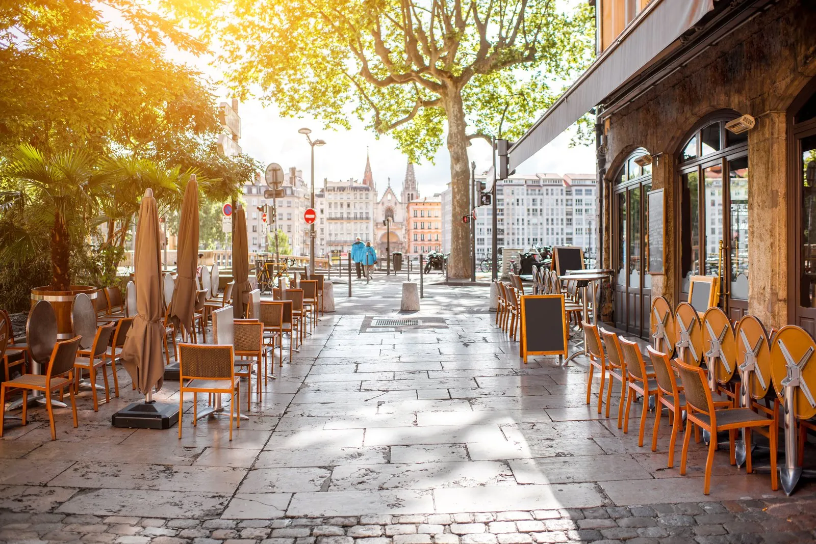 Une terrasse de café dans une rue pavée du centre de Lyon, une église néo-gothique au fond