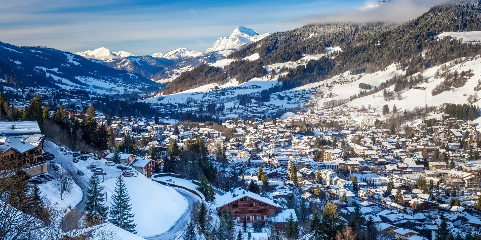 Megève coberta de neve vista do alto: o centro da aldeia, os seus chalés e os cumes dos Alpes no horizonte