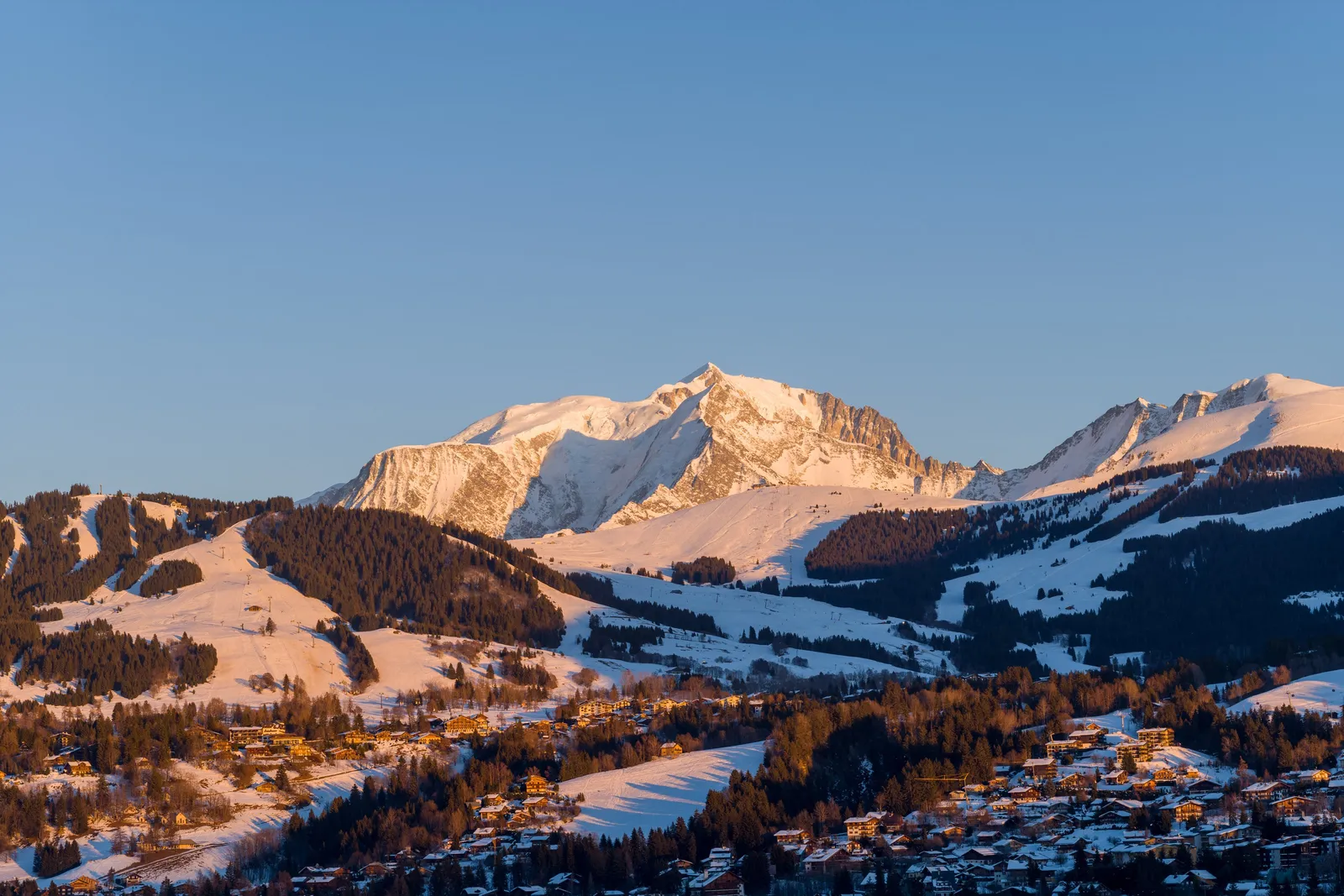Megève e os seus chalés na luz do entardecer, sob o maciço do Monte Branco coberto de neve