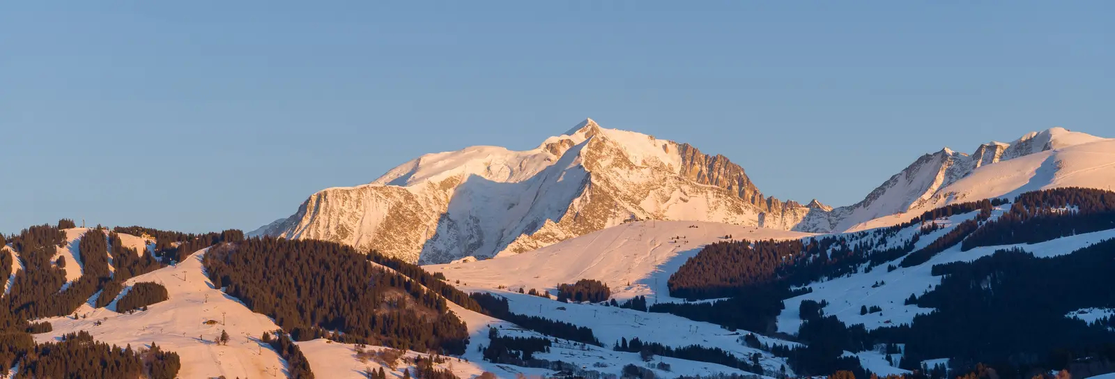 Megève et ses chalets dans la lumière du couchant, le massif du Mont-Blanc enneigé au-dessus