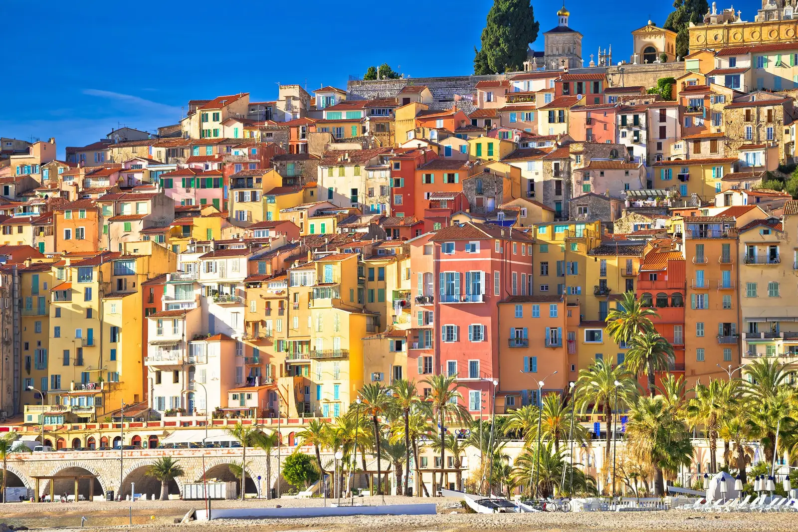 Les façades ocre, jaunes et roses de la vieille ville de Menton, serrées au-dessus des arcades du front de mer et des palmiers