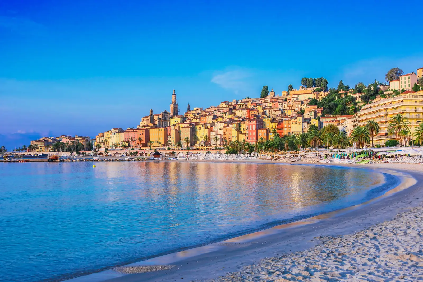 La vieille ville de Menton étagée sur sa colline, son clocher et ses façades pastel au-dessus de la plage, au petit matin