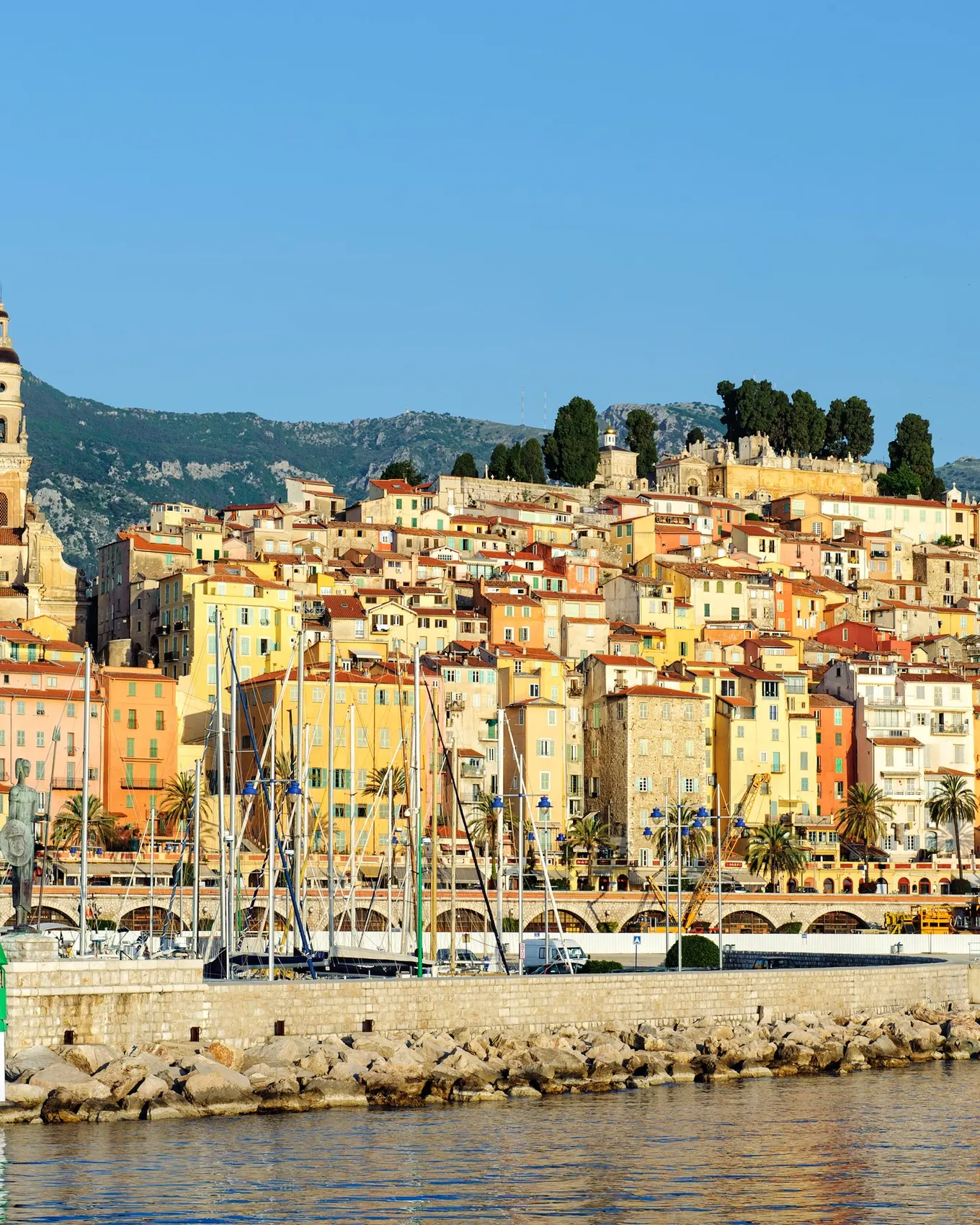 The old town of Menton seen from the harbour: its ochre façades rising up the hill and the bell tower of the Saint-Michel basilica