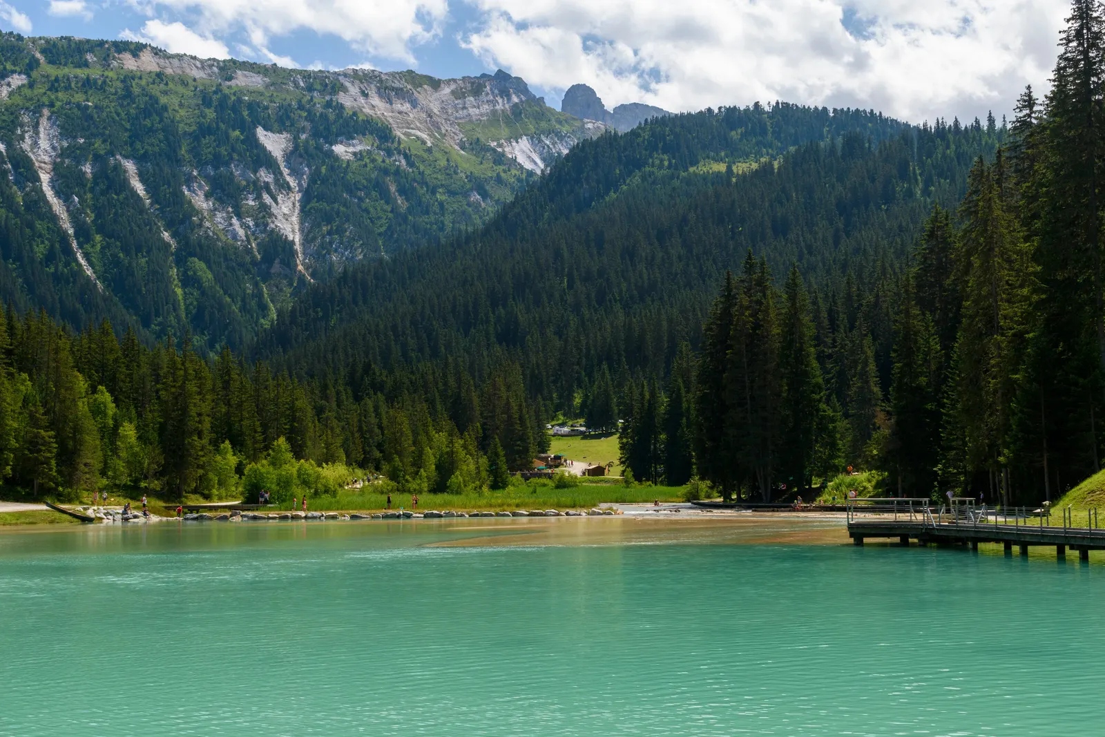 A turquoise lake in Méribel, at the foot of fir forests and mountains, in summer