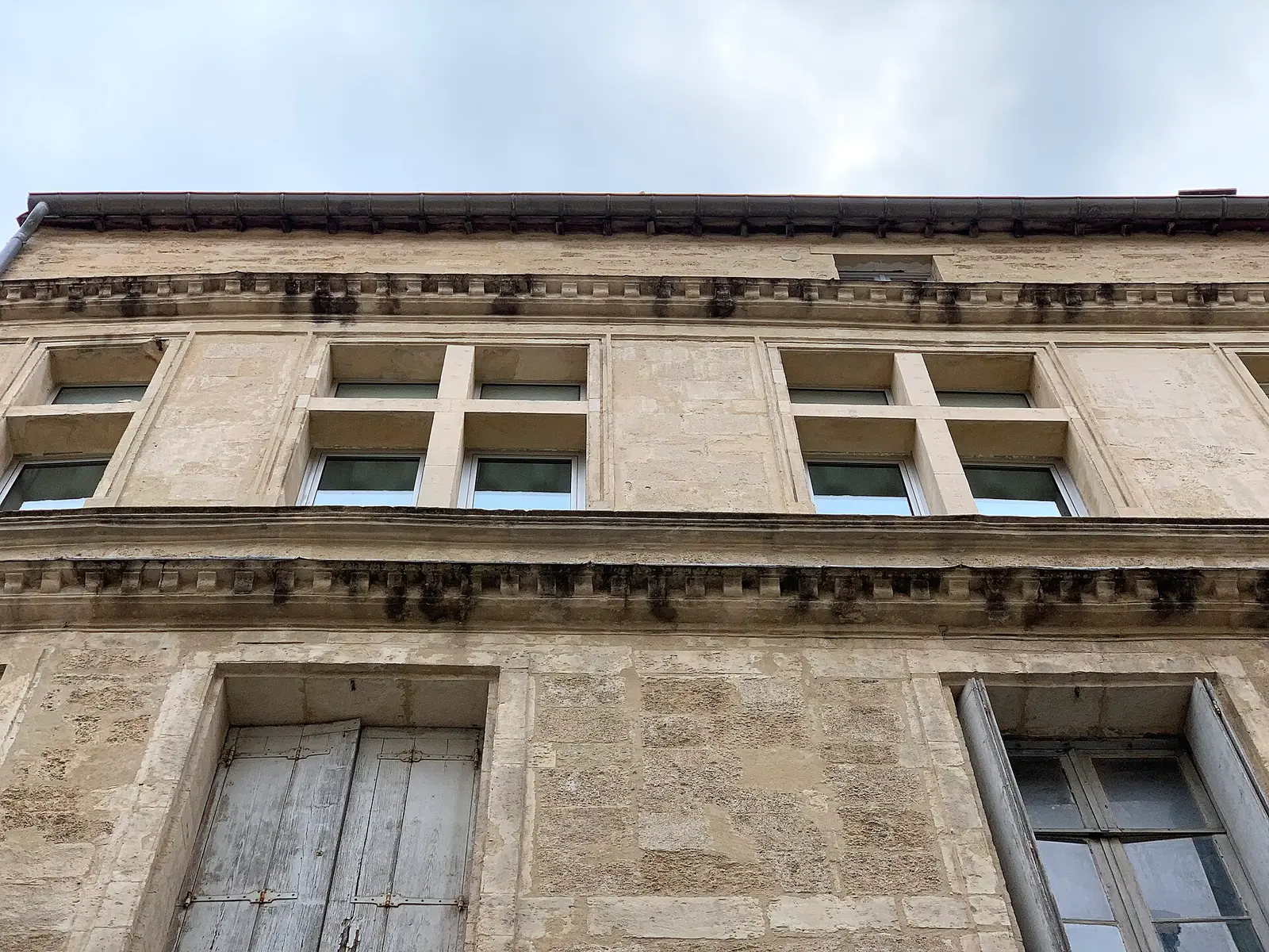 Edifício antigo de Montpellier, pedra clara e janelas de cruzeta sob um céu encoberto