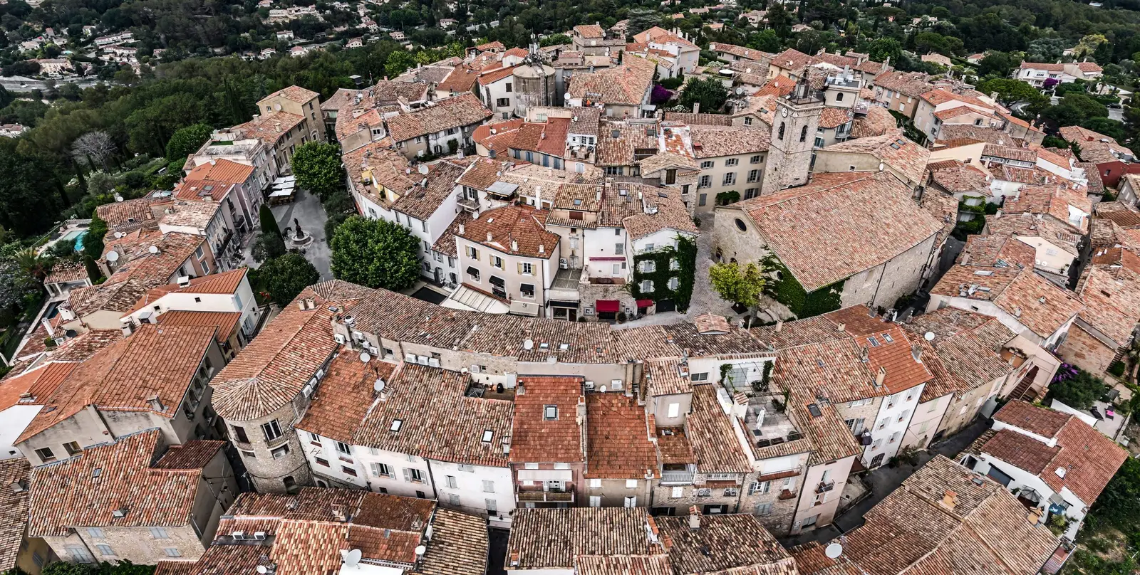 Le vieux village de Mougins vu du ciel, ses toits de tuiles en cercles autour du clocher, dans les pins