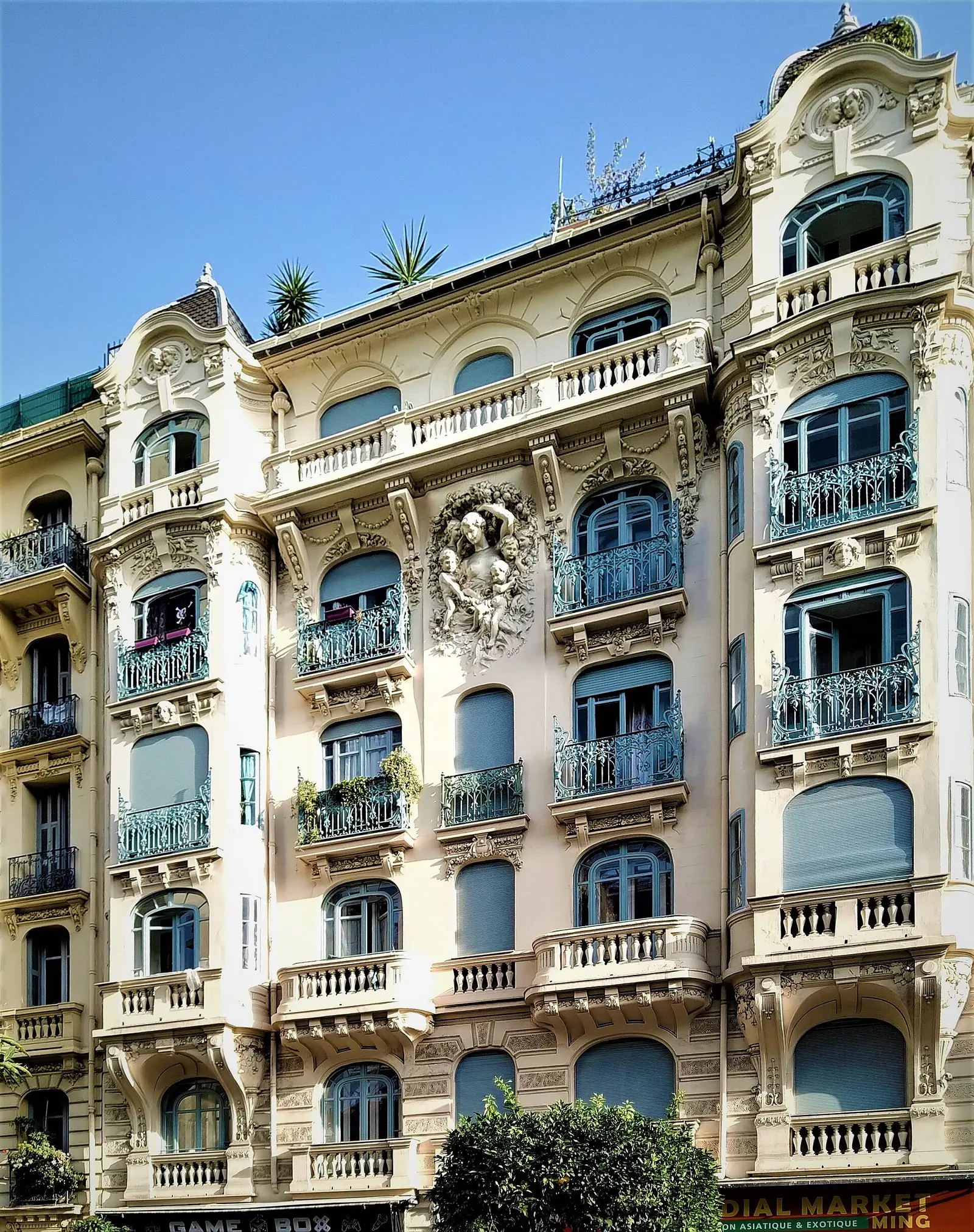 Façade crème et balcons turquoise d’un immeuble niçois aux fenêtres ornementées