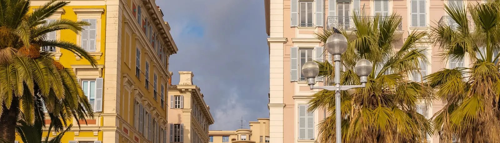 Des immeubles Belle Époque aux façades claires, derrière les palmiers