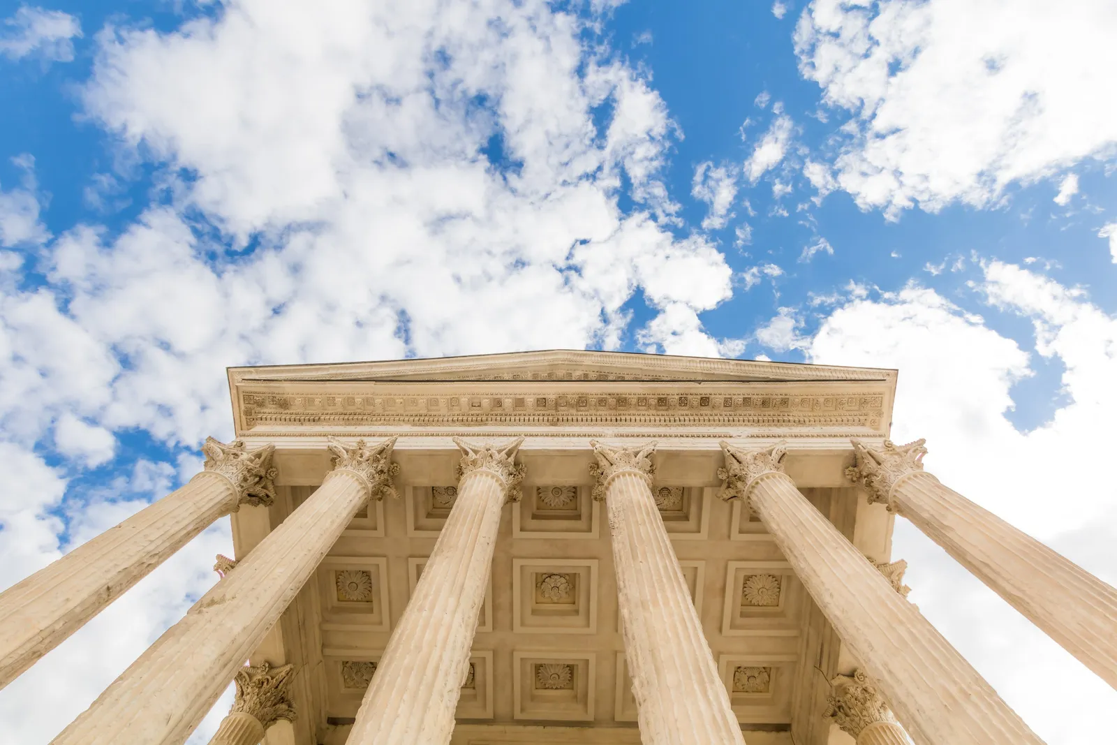 Les colonnes corinthiennes et le fronton de la Maison Carrée, au cœur de l’Écusson, vus d’en bas sous les nuages