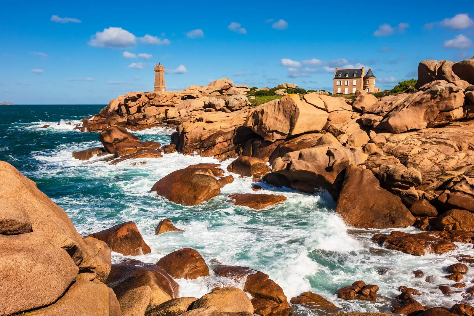Os rochedos de granito rosa de Ploumanac’h em Perros-Guirec, o farol de Mean Ruz e uma mansão acima das ondas que rebentam
