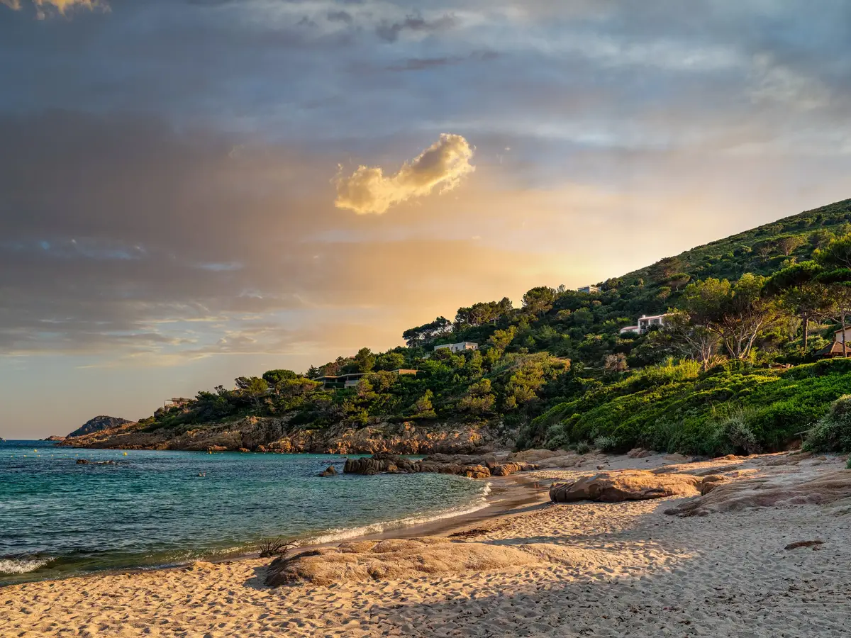 La plage de l’Escalet au couchant, ses rochers et les villas dans les pins de la colline