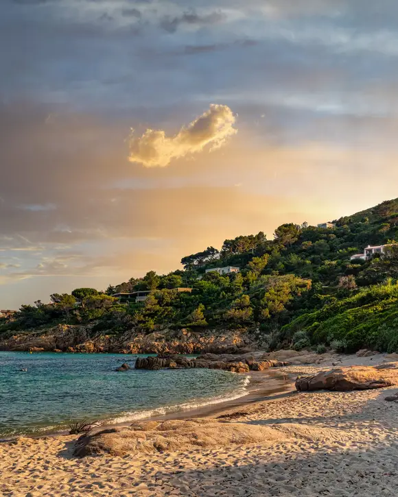 L’Escalet beach at sunset, its rocks and villas among the pines on the hill