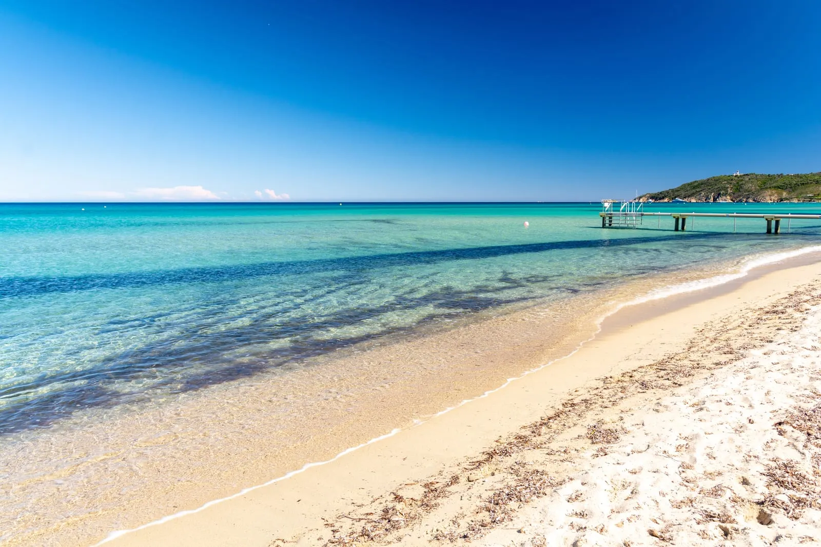 A praia de Pampelonne, a sua água turquesa e um pontão, o cabo Camarat e o seu farol ao longe