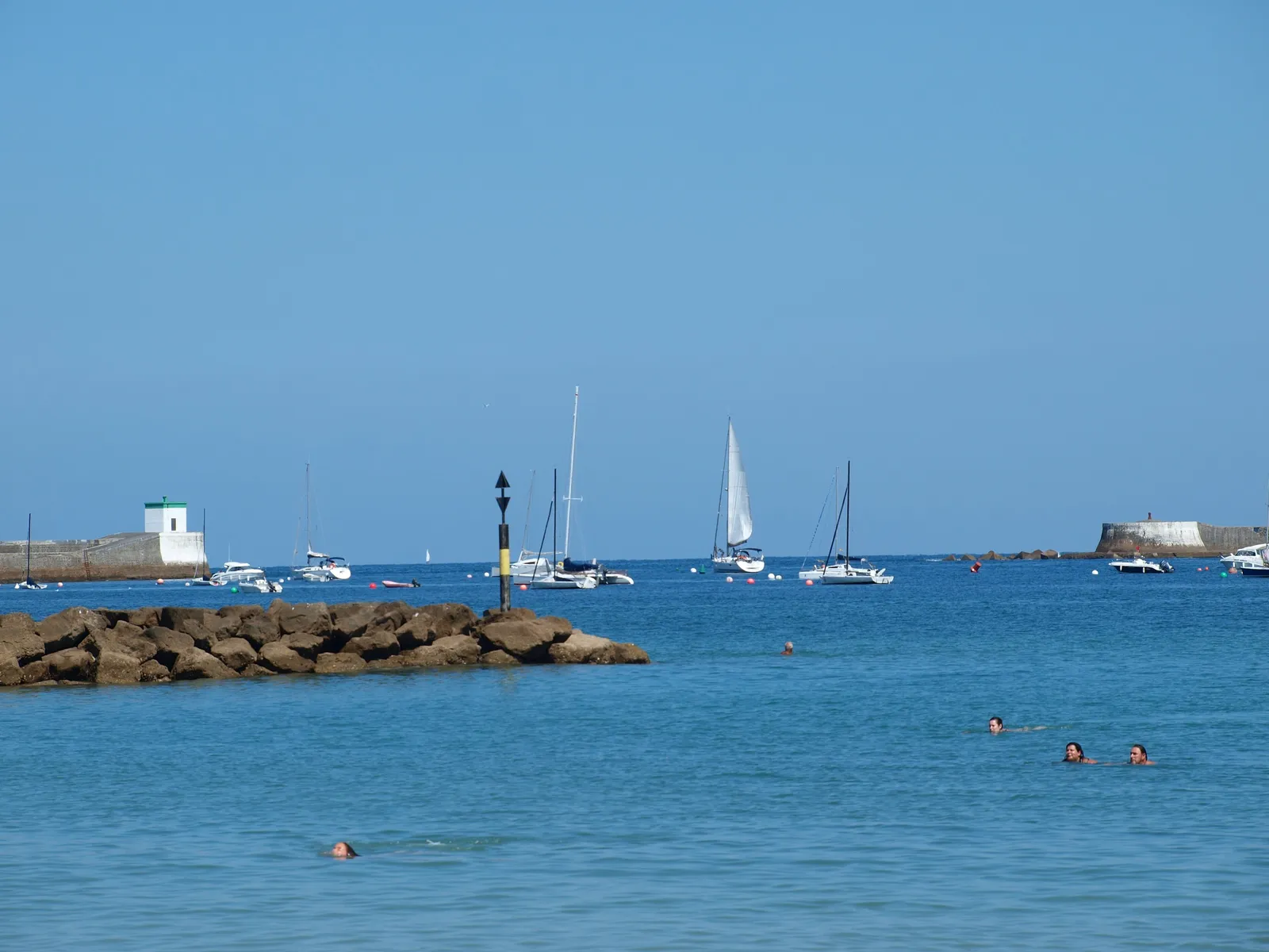 The bay of Saint-Jean-de-Luz, its moored sailing boats, its sea walls and a few swimmers in the blue water
