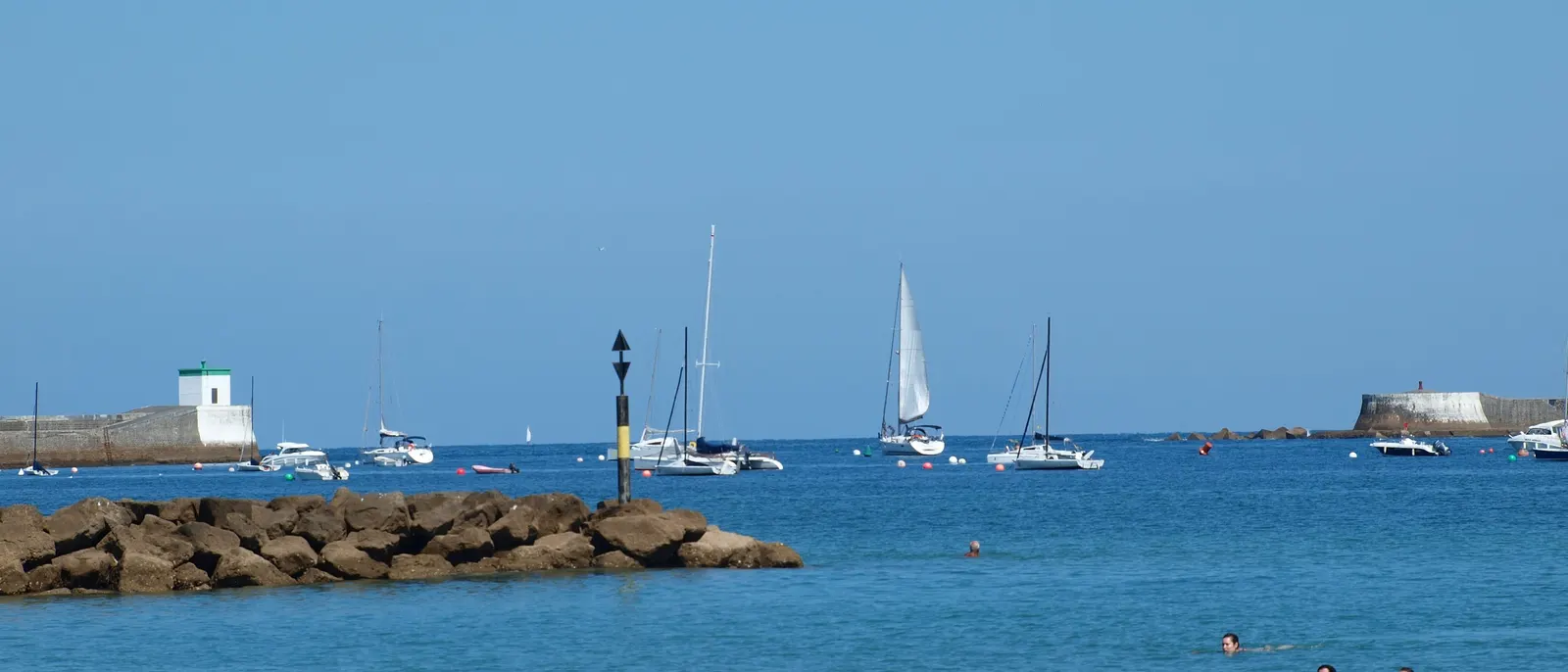 A baía de Saint-Jean-de-Luz, os seus veleiros fundeados, os diques e alguns banhistas na água azul
