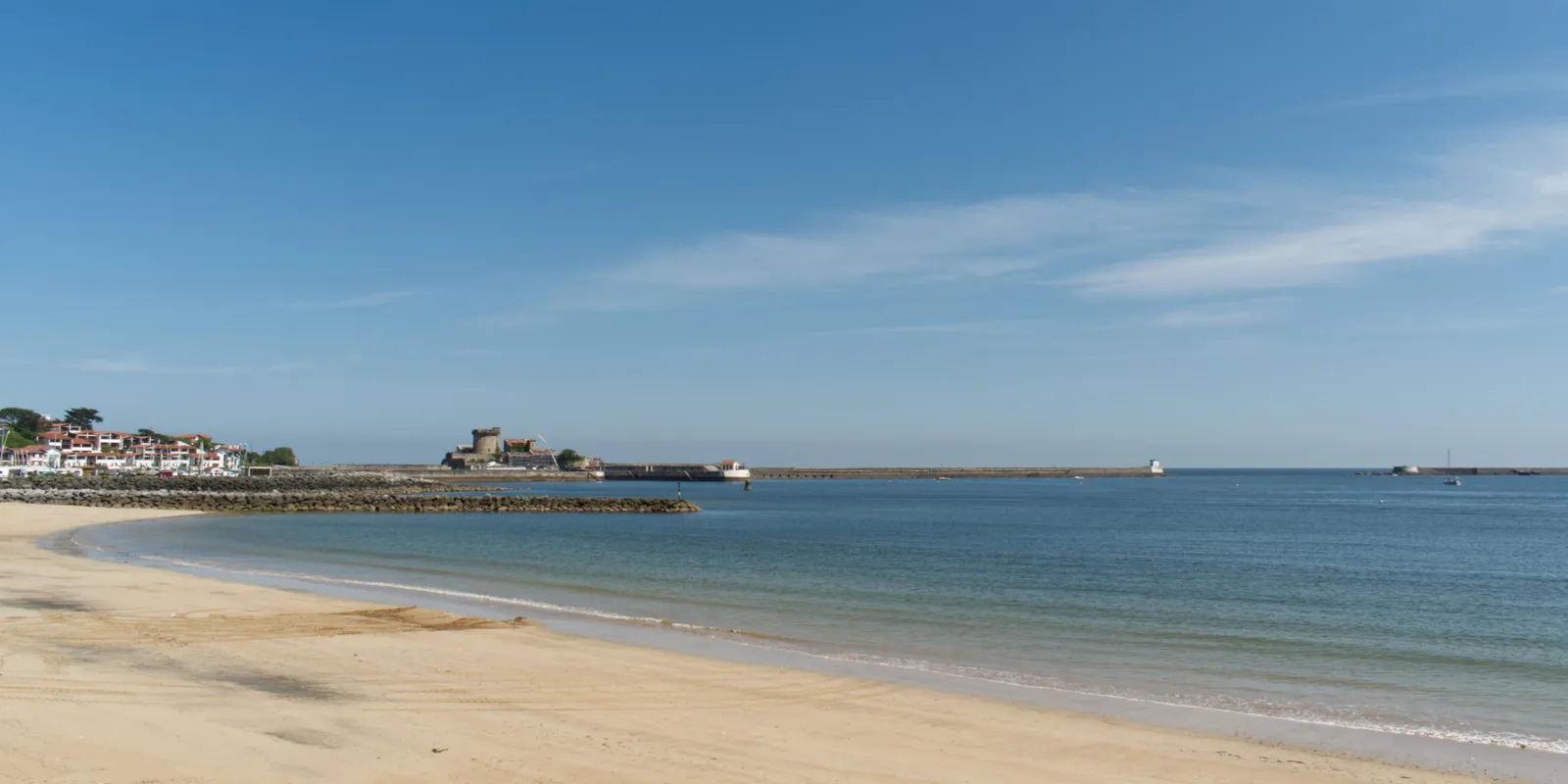 The main beach of Saint-Jean-de-Luz under a clear sky, the calm sea and the bay’s breakwaters in the distance