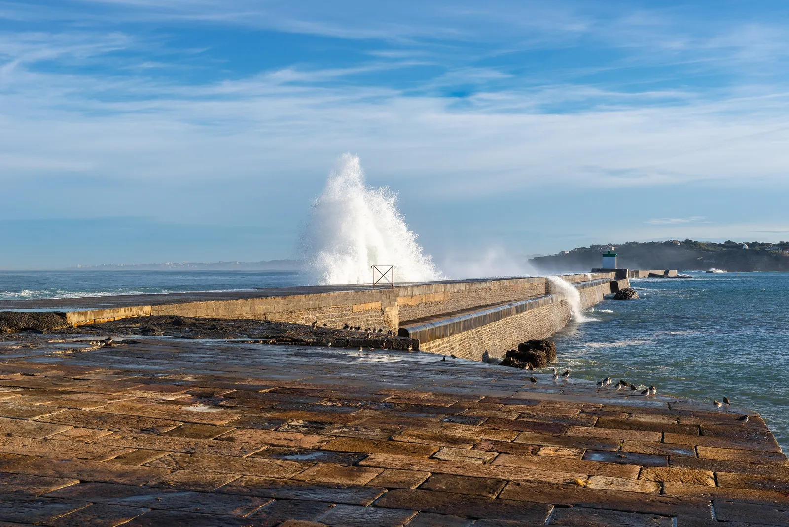 A wave breaking over the sea wall of the bay of Saint-Jean-de-Luz, spray rising above the stone jetty