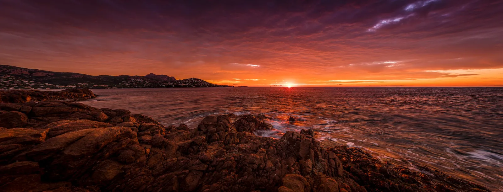 A baía de Agay ao nascer do sol, rochedos de pórfiro em primeiro plano