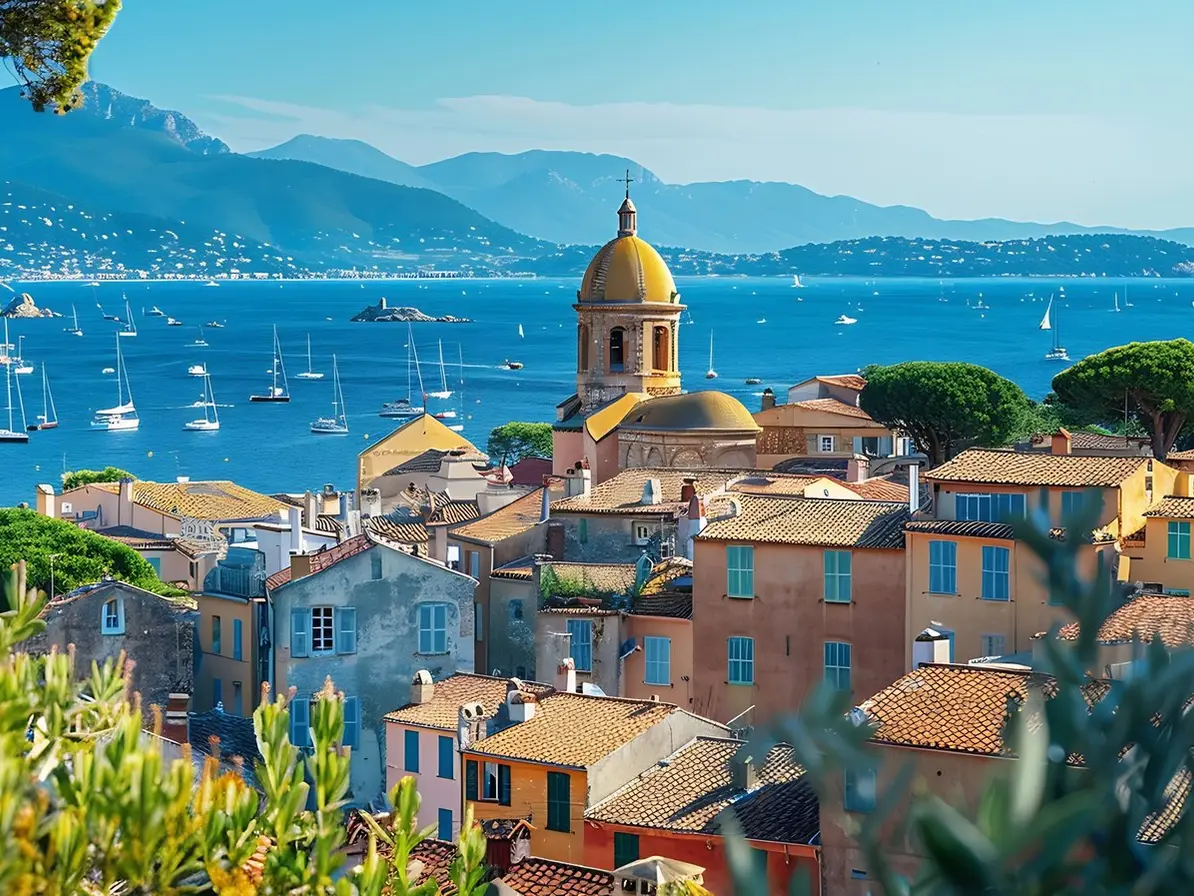 Le clocher de l’église au-dessus des toits, le golfe et ses voiliers au fond