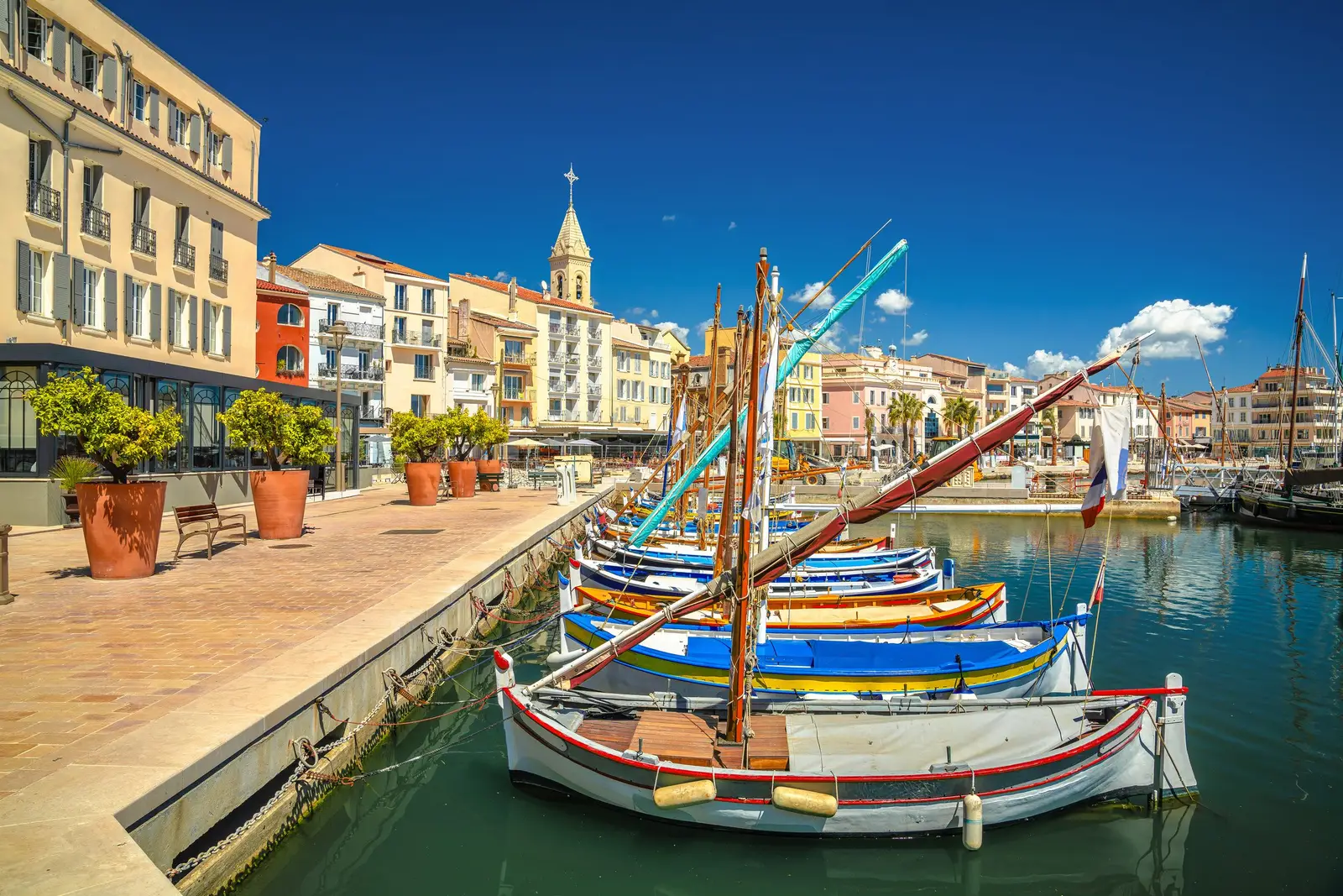 O porto de Sanary-sur-Mer, os seus barcos tradicionais coloridos e as fachadas amarelas dos cais sob o campanário