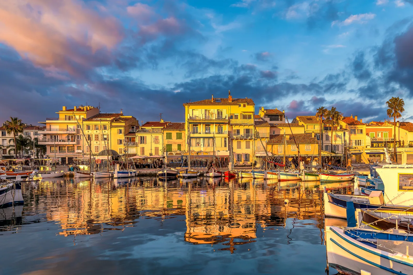 O porto de Sanary-sur-Mer ao pôr do sol, os seus barcos de pesca tradicionais e as suas fachadas amarelas