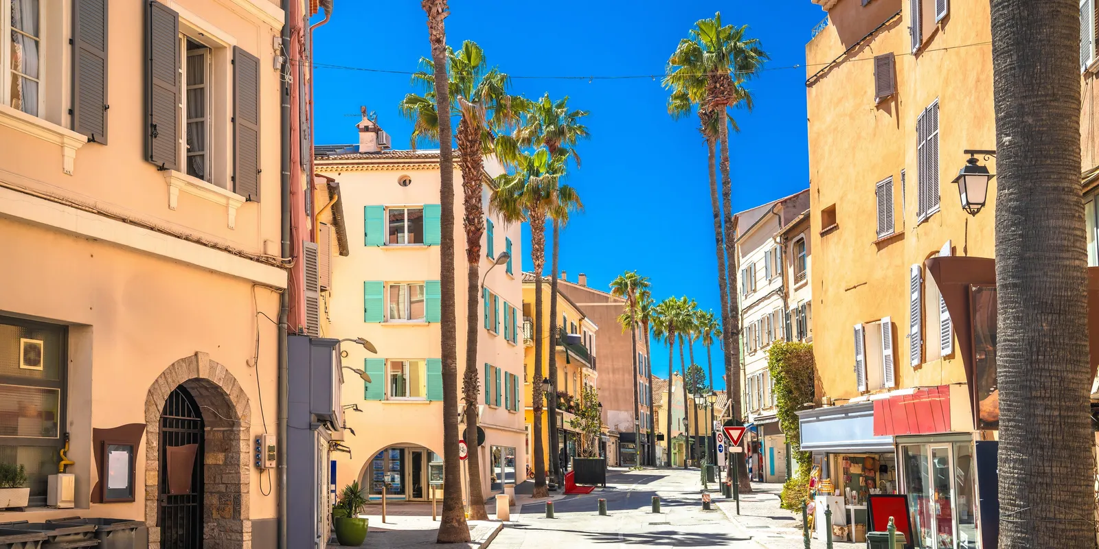 Une rue de Sanary-sur-Mer, ses façades colorées, ses volets et ses palmiers sous le ciel bleu