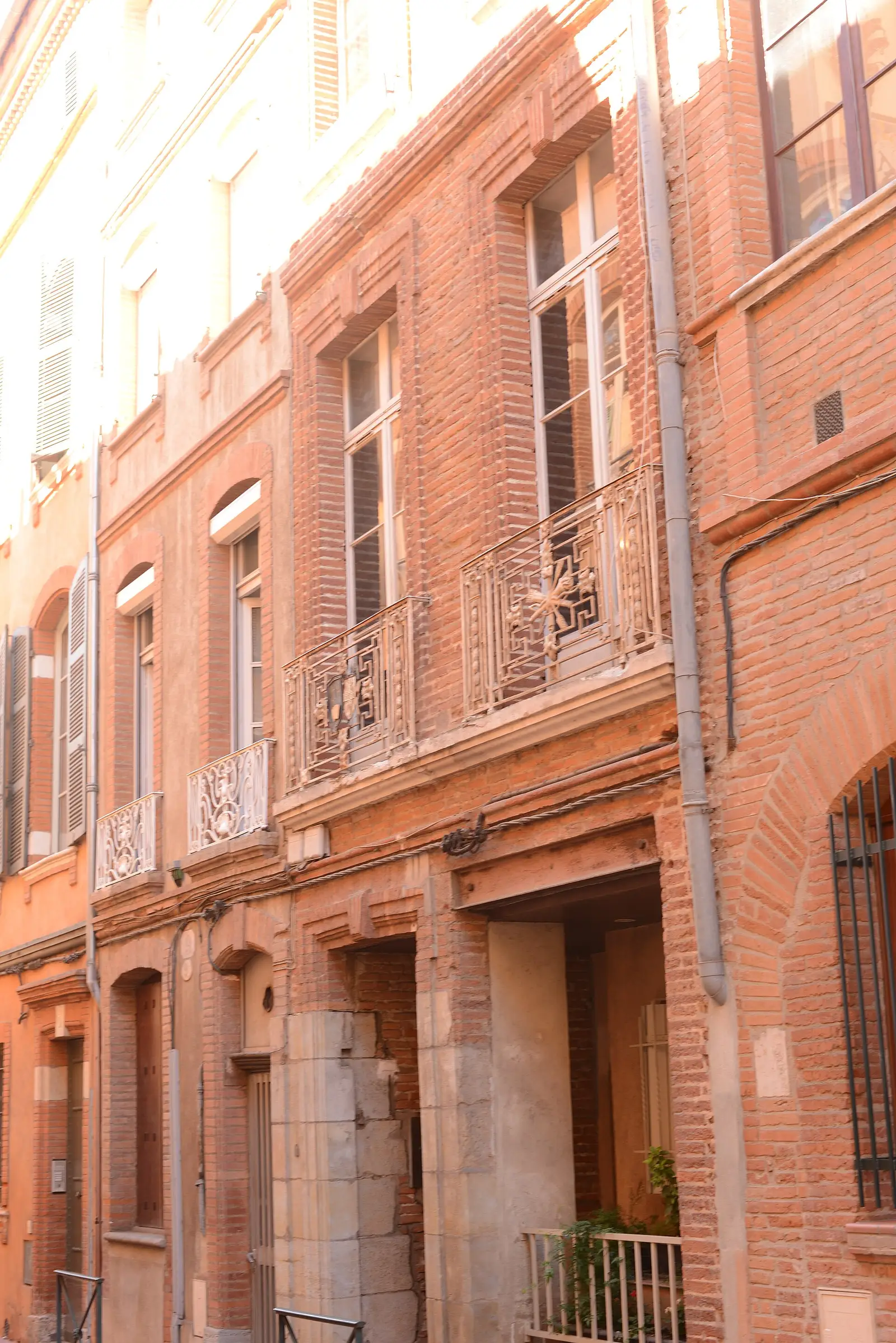 Façade de brique rose de Toulouse dans une rue étroite, balcons blancs en fer forgé