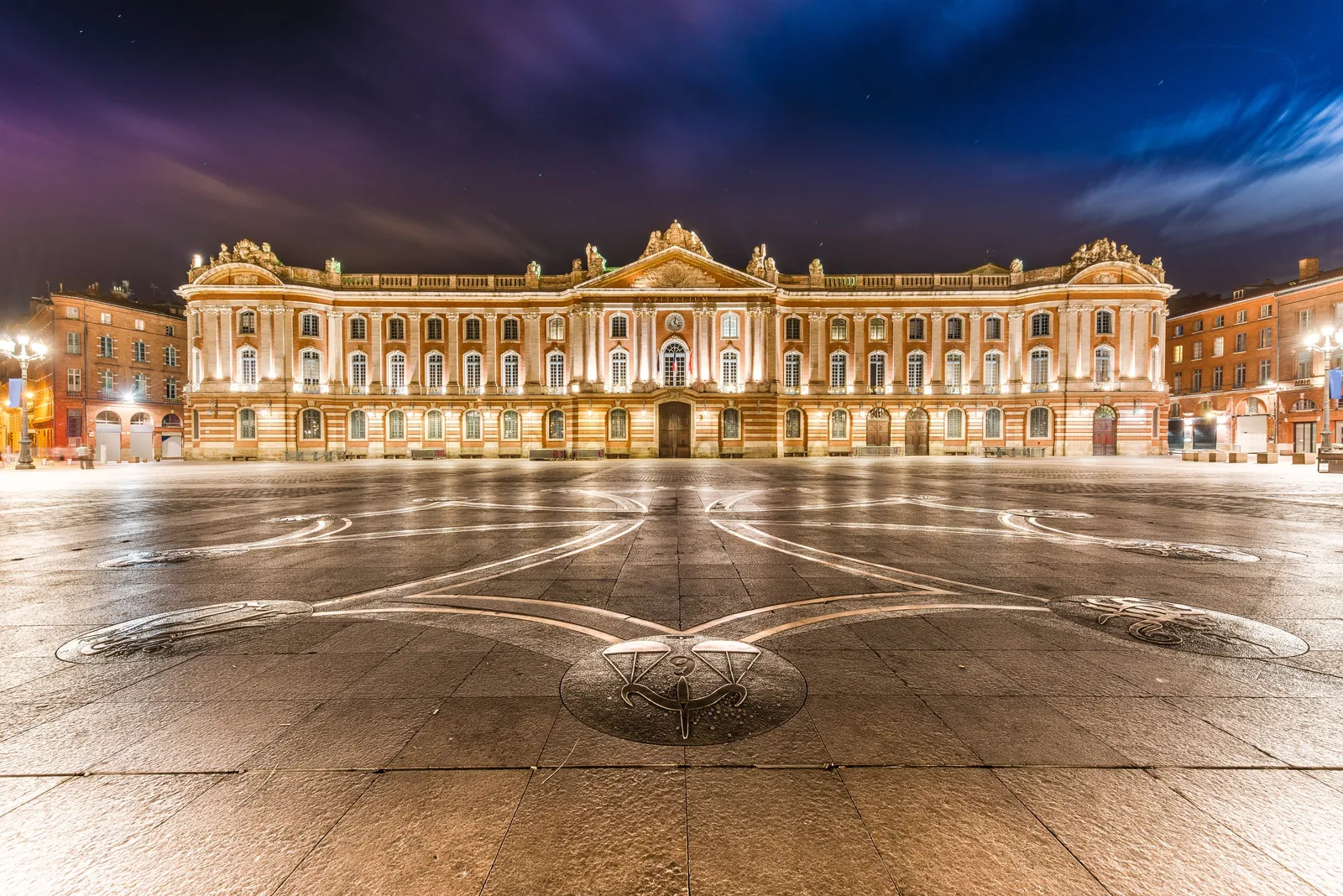 La façade du Capitole illuminée et la croix occitane de la place, la nuit