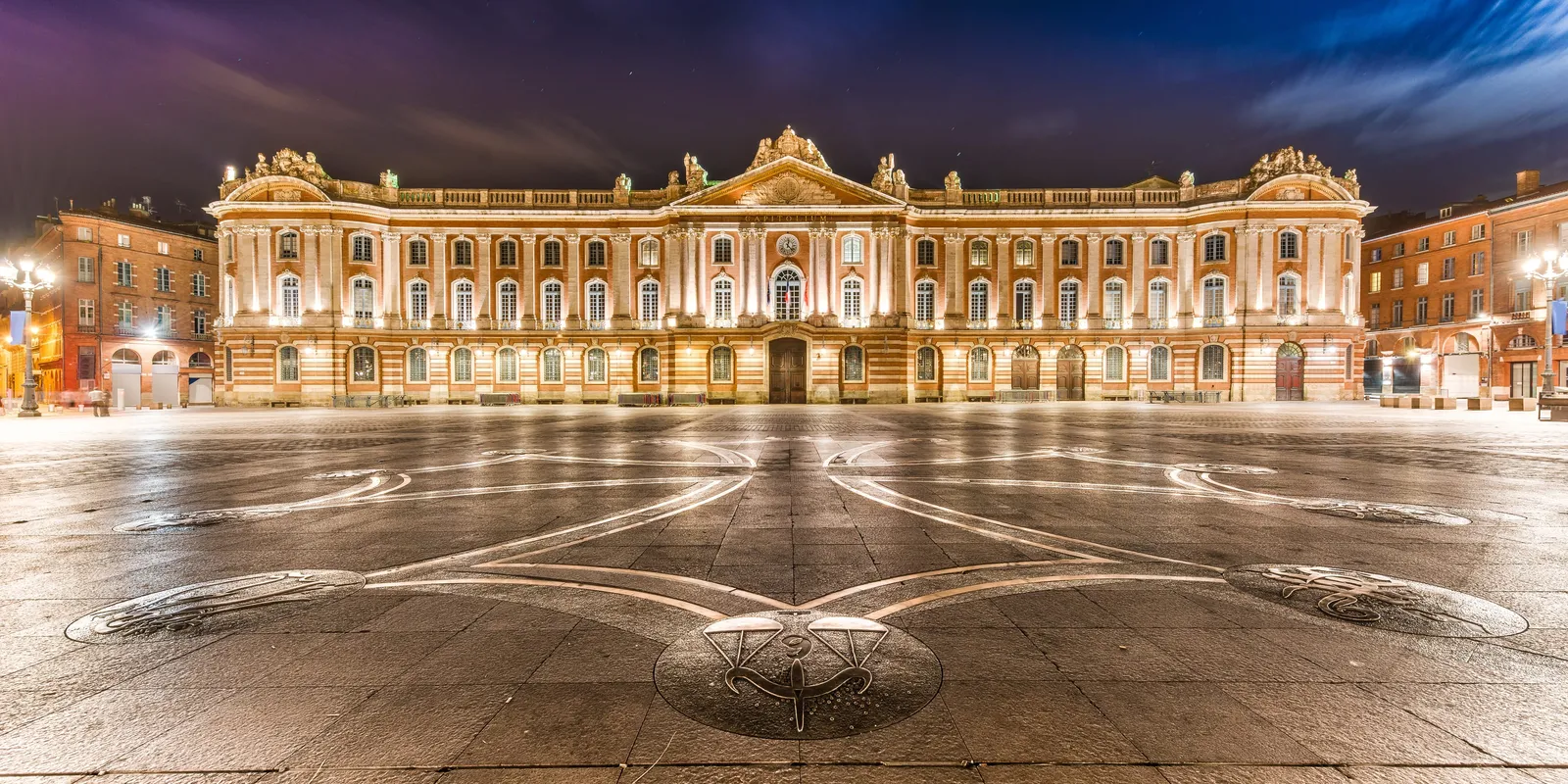 The façade of the Capitole lit up and the Occitan cross on the square, at night