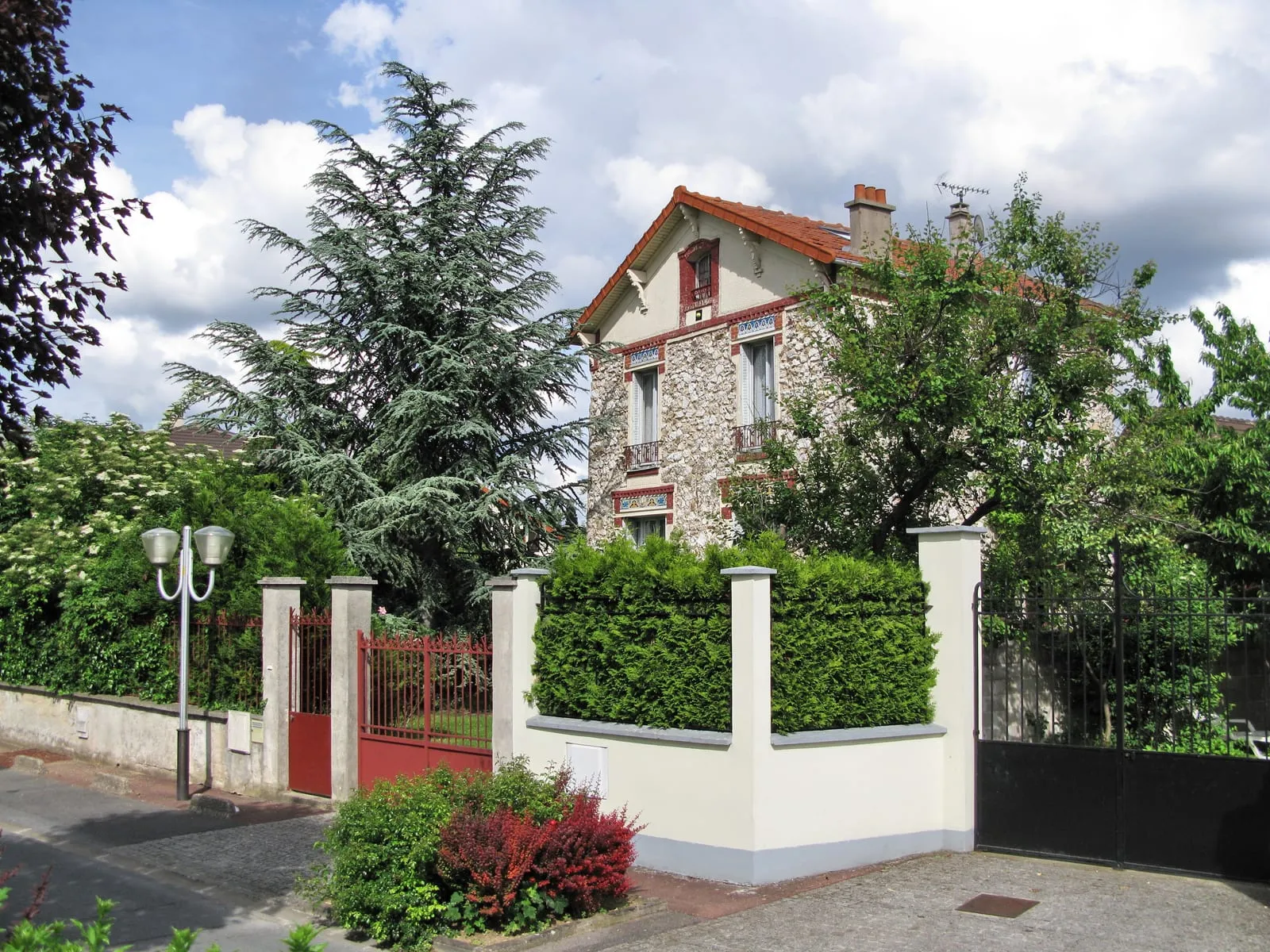 A manor house behind its gate, beneath tall trees