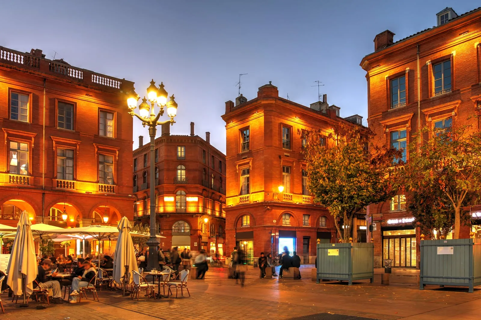 Une place aux façades de brique à la tombée du jour, ses terrasses de café
