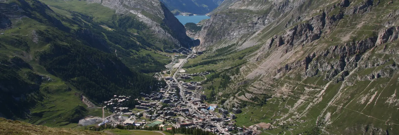 Val-d’Isère vu des hauteurs en été, le village-centre au fond de la vallée de l’Isère et les sommets enneigés au loin