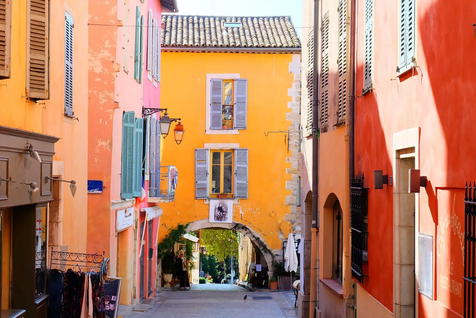 Une ruelle du vieux Valbonne et ses façades ocre, rose et orange, ses volets bleus et une arche de pierre au bout de la rue