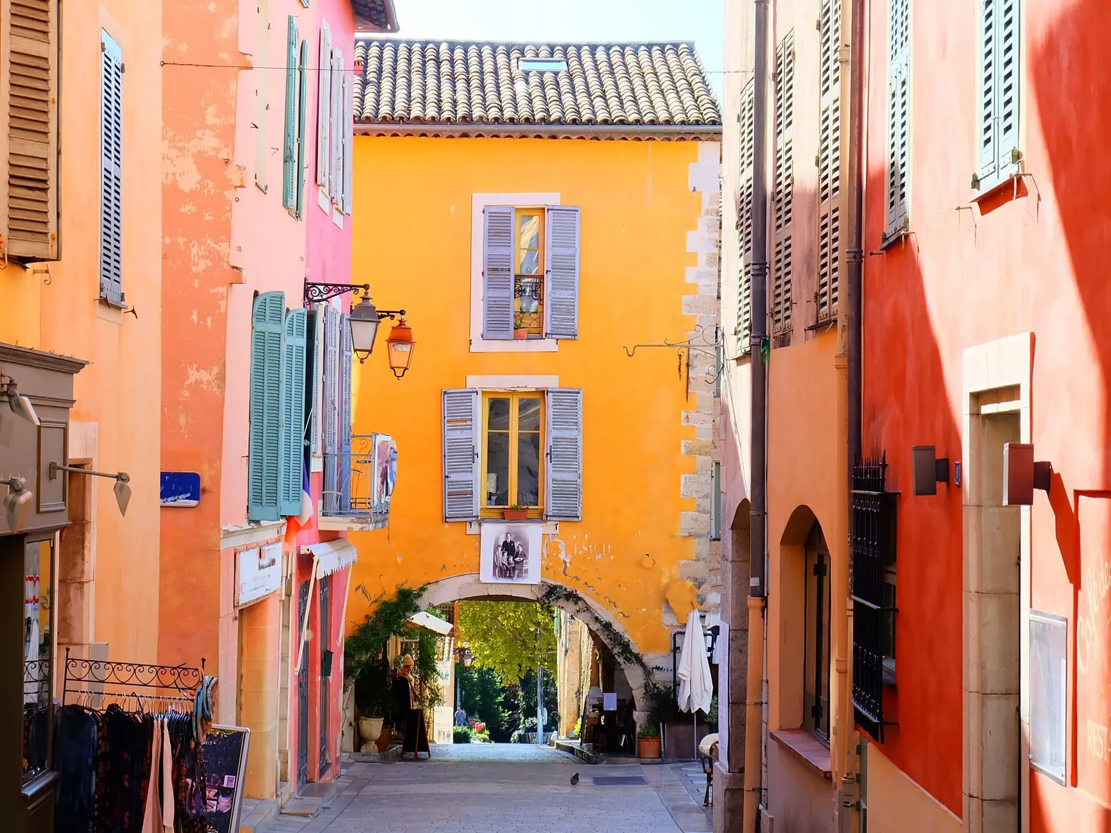 Uma ruela do velho Valbonne com as suas fachadas ocre, rosa e laranja, as suas portadas azuis e um arco de pedra ao fundo da rua
