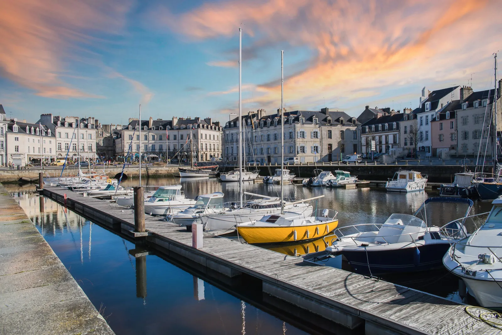 Sailing boats moored at the pontoons of Vannes harbour at sunset, in front of the quayside façades under a pink sky